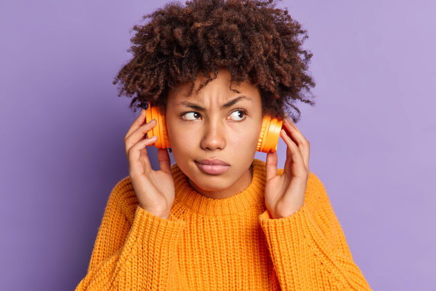 皱眉严肃的非洲裔美国年轻女子的特写肖像 聆听音轨集中在某处 戴着无线耳机摆姿势智能种族时髦