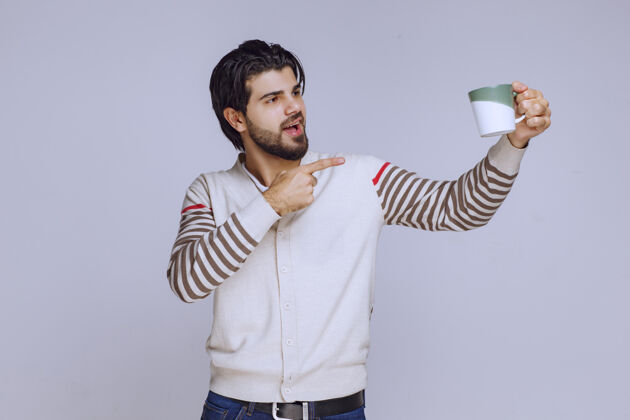 年轻人一个穿着白衬衫的男人拿着一个咖啡杯展示给大家看人成人年轻