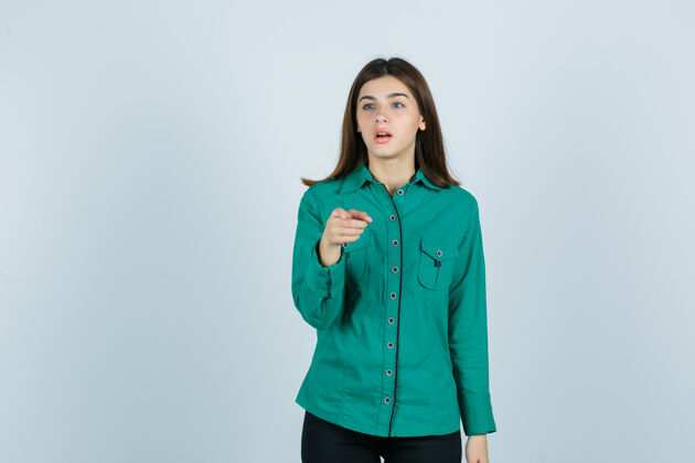 商务年轻的女性指着镜头 一边看着远处的绿色衬衫 看着震惊 前视图手势嘴巴表情