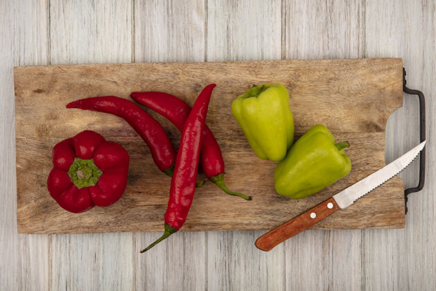 烹饪顶视图彩色铃铛和辣椒上的一个木制厨房板与刀在灰色的木制表面新鲜辣椒蔬菜