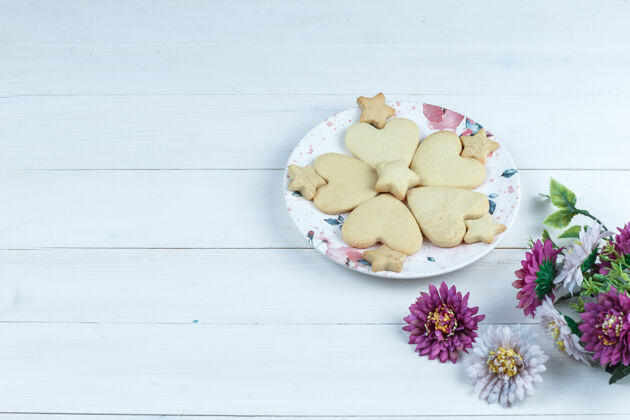 面包屑高角度观看心形和星星饼干在白色盘子与鲜花堆叠糖心