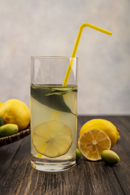 果汁健康的柠檬汁在一个玻璃与柠檬和金盏花的柳条托盘上的一个白色表面上的木桌侧视图玻璃餐桌水果