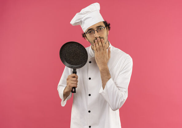 眼镜年轻的男厨师穿着厨师制服戴着眼镜拿着煎锅捂着嘴年轻厨师粉红