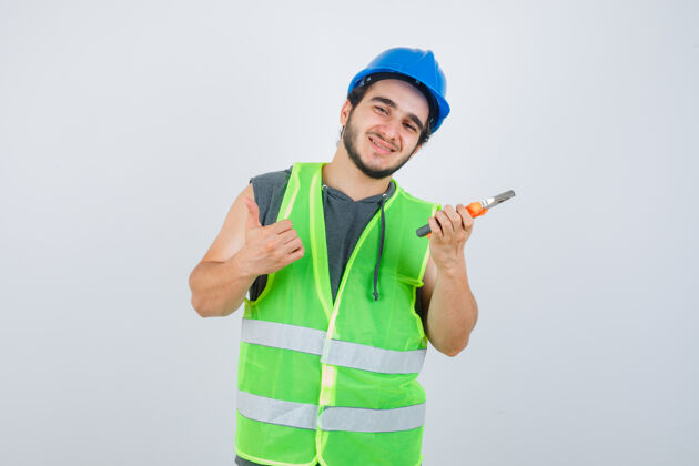 学校年轻的建筑工人穿着工装 拿着钳子 同时竖起大拇指 看上去很快乐 正对着窗外小学男人英俊