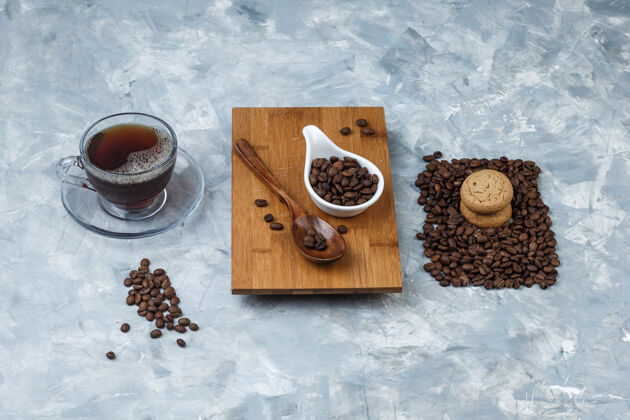 热高角度观看咖啡豆 木制勺子放在砧板上与饼干 咖啡杯放在浅蓝色大理石背景上水平乐趣香味饼干