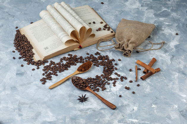 浓缩咖啡一些咖啡豆和磨碎的咖啡 书 香料 麻袋在一个木制勺子上的灰色背景 高角度的看法能量食物