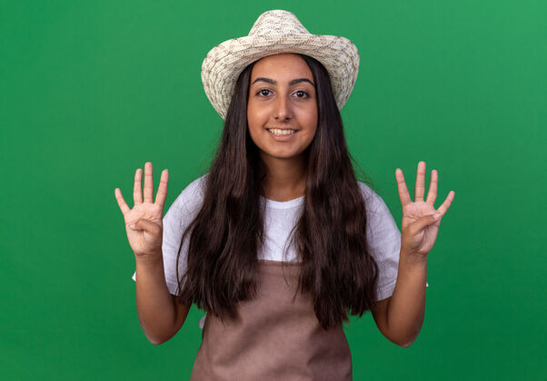 年轻人穿着围裙 戴着夏帽的年轻园丁女孩微笑着站在绿墙上的八号人物帽子围裙花园