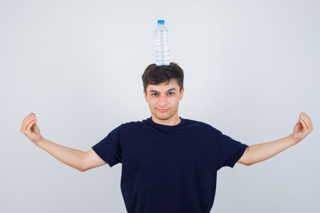 成人一个身穿黑色t恤的年轻人头上顶着一瓶水 做着意大利式的手势 看上去很自信 前视前面男人模特