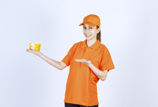 员工穿着黄色制服的女快递员拿着一个外卖面杯子指着它休闲服装人体模特
