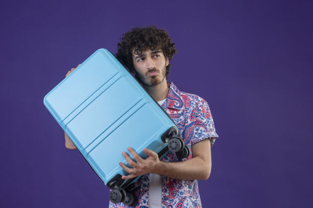 帅气体贴的年轻帅气的卷发旅行者拿着手提箱 看着右边有复制空间的紫色隔离墙抱着年轻右边