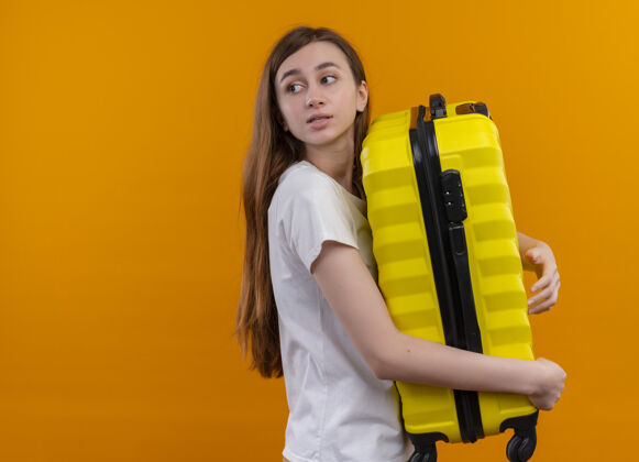 左边年轻的旅行家女孩拿着手提箱 在孤立的橘黄色墙壁上看着左边的复制空间手提箱年轻人拿着