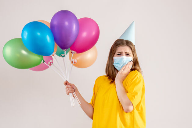 健康戴着白色面具手持彩色气球的年轻女性气球流行病生日