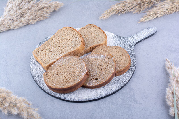 面团在大理石表面的羽毛草杆旁边 铺着面包片的面粉板饮食黑麦切片