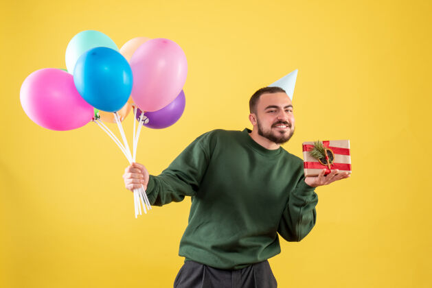 背景正面图：手持彩色气球的年轻男性 背景为黄色公园气球礼物