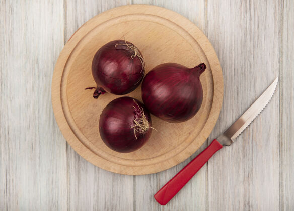 洋葱红色洋葱的顶视图在一个木制的厨房板上 刀放在灰色的木墙上木板桌子特写