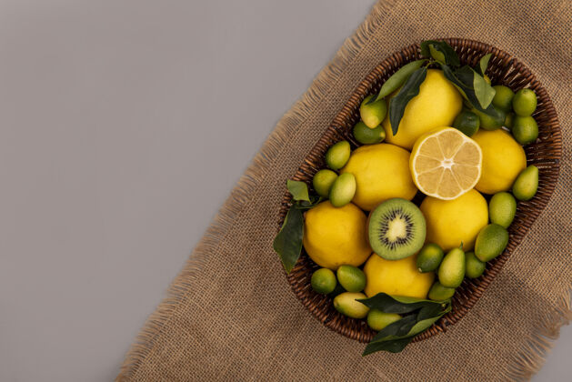 膳食顶视图新鲜水果 如猕猴桃金盏花和柠檬桶上的麻袋布上的灰色墙壁复制空间柠檬水果猕猴桃