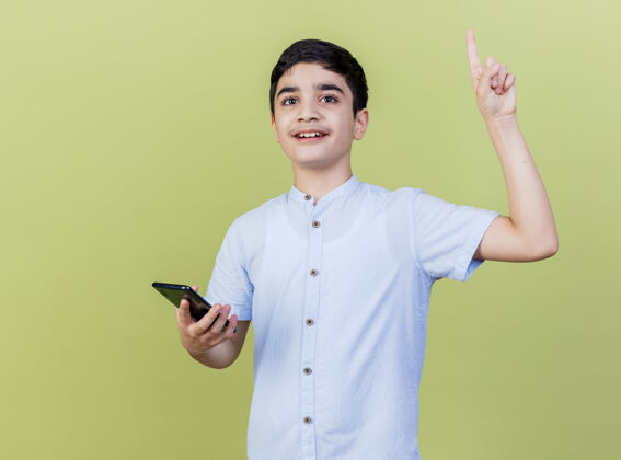 拿着印象深刻的小男孩拿着手机看着前面指着孤立的橄榄绿墙上印象人市民