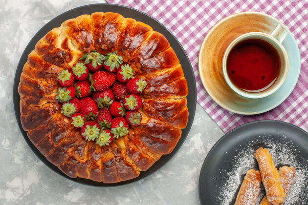 新鲜白色桌子上有美味的草莓派 新鲜的红色草莓和一杯茶派美味顶视图