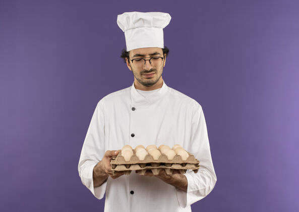 思考想着年轻的男厨师穿着厨师制服 戴着眼镜 拿着紫色的鸡蛋看着一批批批年轻厨师