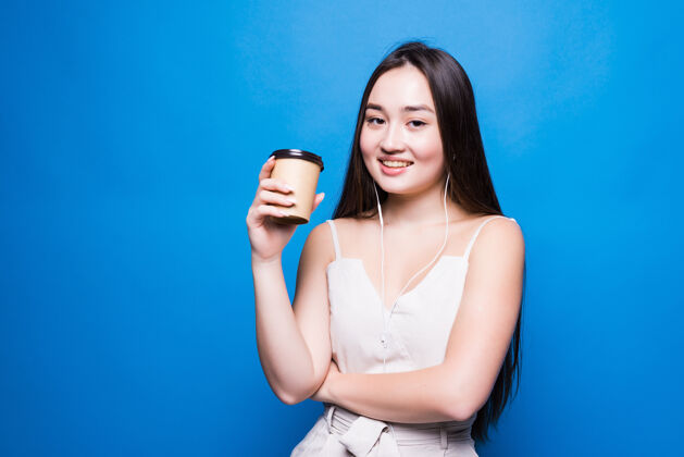 剪微笑着拿着外卖咖啡杯的亚洲年轻女子孤零零地站在蓝色的墙上外卖快乐韩语
