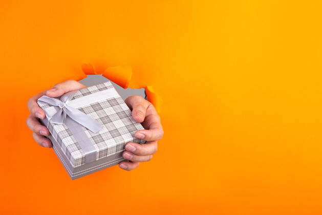 包装一只手拿着一份礼物穿过一张橙色的破纸洞手撕破