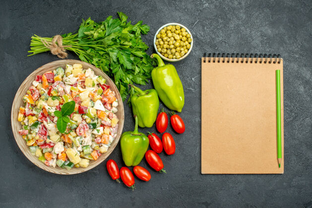 食物深绿色桌子上一碗蔬菜沙拉的顶视图 旁边有蔬菜和记事本生菜饮食素食