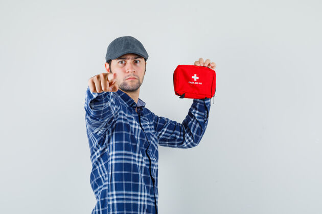 套装一个穿着衬衫 戴着帽子的年轻人指着摄像机 手里拿着急救箱 表情严肃成功休闲男人