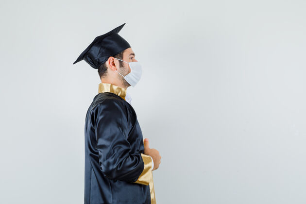 礼服穿着研究生制服的年轻人拿着他的长袍 看上去很体贴男人男人毕业