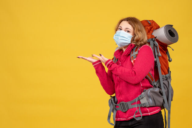 成人俯视图：戴着医用面罩的年轻旅行女孩正在收拾行李 并指向右边的东西指漂亮肖像