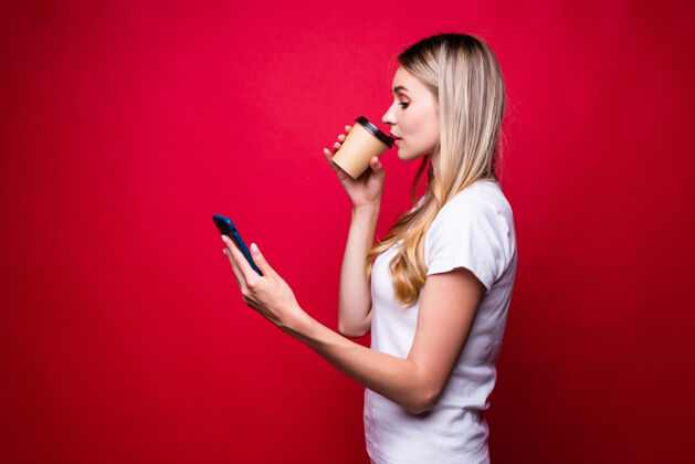 脸在红墙上 一个金发女人拿着一杯外卖咖啡在打电话交流杯子冬天