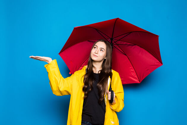 中年穿雨衣的年轻女子拿着五颜六色的伞在蓝色的墙上模特自信老年人