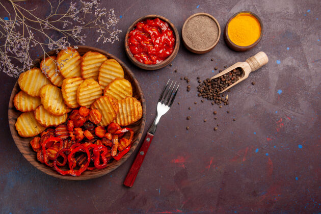 生的顶视图烤土豆与熟蔬菜和调味品在黑暗的空间调味品美味烹饪