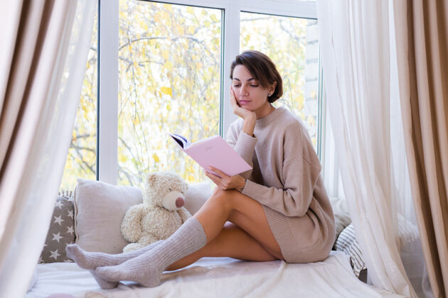 十二月家里的女人拿着笔记本坐在窗台上 穿着舒适的毛衣和温暖的羊毛袜 窗外很冷窗户房子枕头