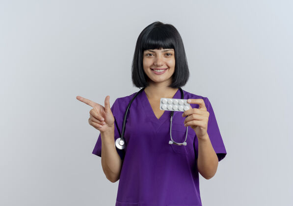 壁板面带微笑的年轻黑发女医生 穿着制服 手持听诊器 指着旁边的药微笑制服听诊器