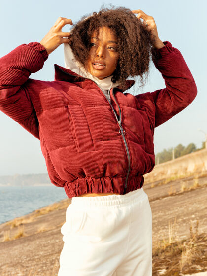 凝视穿着红色夹克和现代白色裤子的非洲女孩 时尚的外表灿烂灿烂的笑容 苗条的身材 卷卷发秋天寒冷的天气 温暖的衣服户外自然风格女性