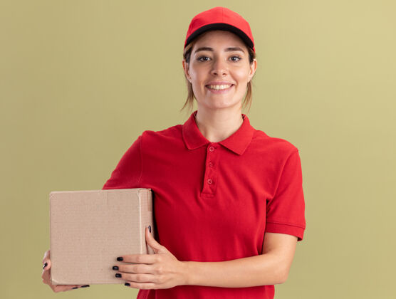 摆姿势身着制服的年轻漂亮的送货女孩微笑着拿着橄榄绿的名片盒年轻送货漂亮