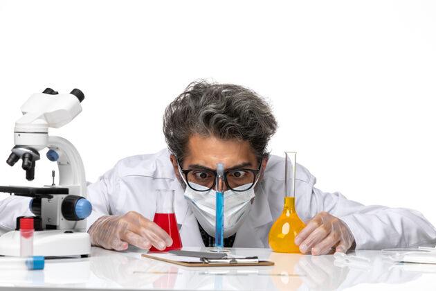 科学正面近距离观察穿着特殊套装的中年科学家 他们拿着解决方案坐在白色背景上 看着它们 男性病毒科学化学化学医学坐姿