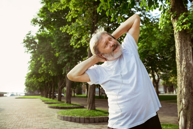 乐趣高级男子在城市街道上跑步高加索男模在夏天的早晨慢跑和有氧训练在草地附近做伸展运动健康的生活方式 运动 活动理念健身跑步树