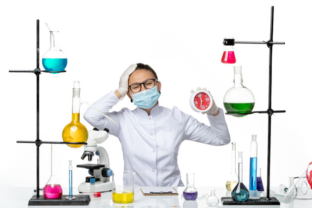 医学前视图：穿着医疗服的女化学家 戴着面具 拿着白色地板上的时钟病毒实验室化学冠状病毒-飞溅医生视图前面