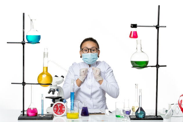 实验室前视图穿着医疗服的女化学家带着面罩坐在桌子前 溶液背景为浅白色病毒化学实验室的covidsplash实验室病毒科学