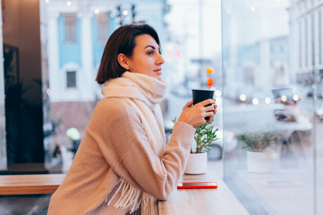 年轻一个女孩在舒适的咖啡馆里用一杯热咖啡取暖马克杯坐着街道