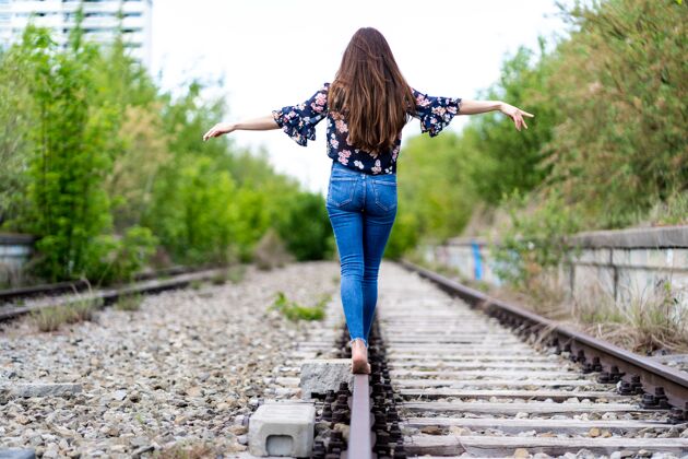 腿一个年轻的女性赤脚穿过火车铁轨 试图保持平衡黑色铁路白色