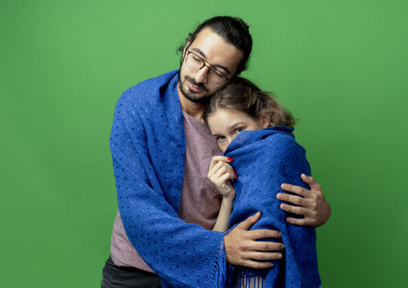 亲爱的一对年轻的男女 幸福的男人拥抱着他心爱的女友 把她裹在温暖的毯子里 站在绿色的背景上情侣毯子年轻