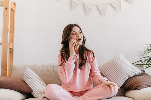 女人一个穿着粉色睡衣的女人坐在沙发上 枕着柔软的枕头 一边打电话休息肖像玩家