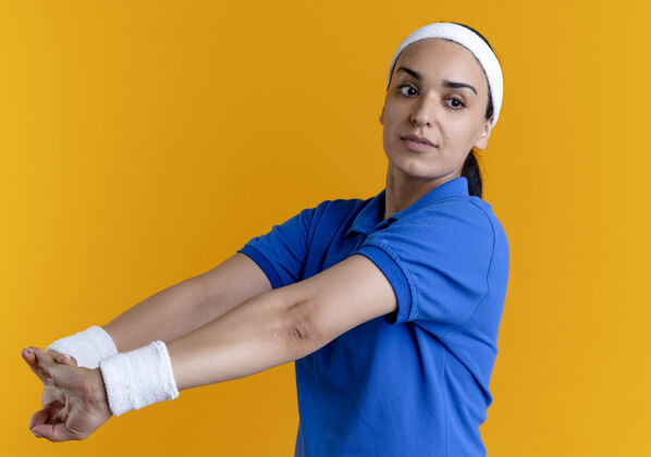 运动年轻自信的高加索运动女性戴着头带和腕带 双手笔直地握在一起 看着橙色背景上孤立的一面 还有复制空间头带壁板直
