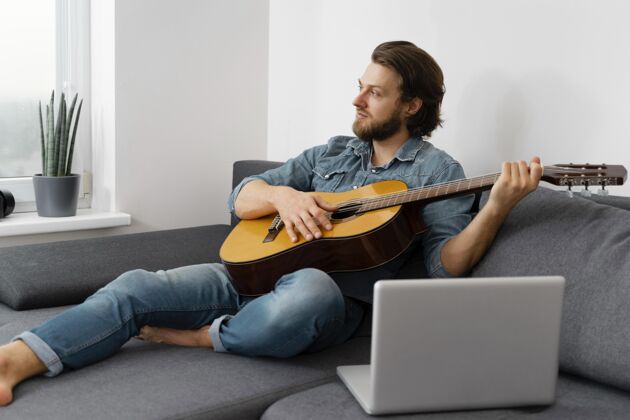 在家里在家弹吉他的全明星男人室内设备笔记本电脑