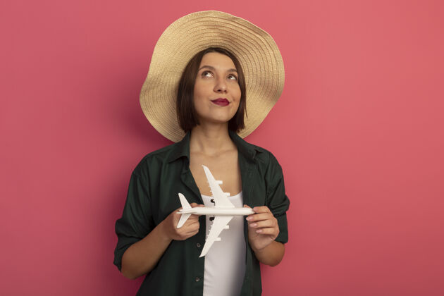 拿着戴着沙滩帽的漂亮女人抱着飞机模型 孤零零地仰望粉红色的墙上感觉站海滩