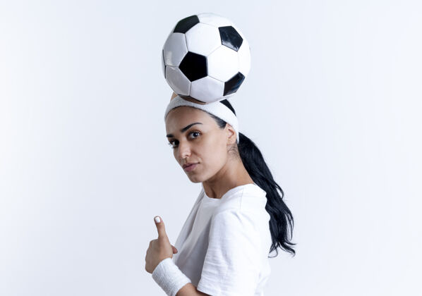 腕带年轻自信的高加索运动女性戴着头带和腕带站在一边 将球举过头顶 大拇指竖起 在白色背景上与复制空间隔离侧头带年轻
