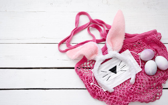 检疫复活节静物与粉红色的字符串袋 装饰复活节兔子耳朵 医疗面具和鸡蛋在木制表面静物流行病传统