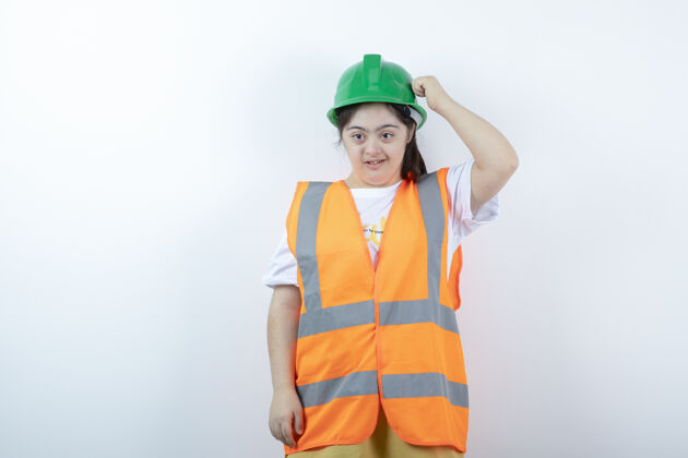 表情戴着安全帽的年轻女建筑工人站在白墙上制服职业姿势